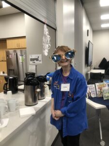 Person wearing novelty oversized sunglasses in a kitchen area next to a beverage station and book display.