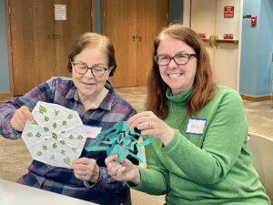 Two people smiling while holding paper snowflakes.