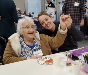 Two people smiling and holding hands at a table with craft supplies.