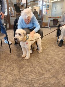 Older woman petting a fluffy cream-colored dog indoors.