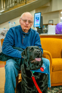 Man sits in a chair behind a black dog