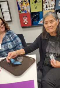Person holding a blue butterfly on a tray with colorful art pieces in the background.