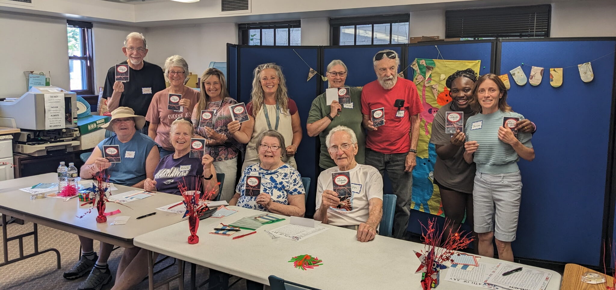 Cafe attendees smile and hold up patriotic cards they made at memory cafe