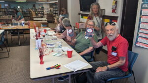 Participants seated at a table smiling and holding up hand crafted cards
