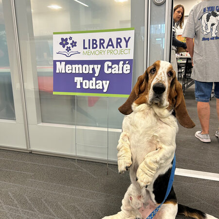 A beagle dog standing on its hind legs next to a Memory Cafe sign